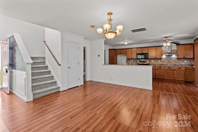 kitchen featuring crown molding, hardwood / wood-style floors, ceiling fan with notable chandelier, wall chimney exhaust hood, and pendant lighting