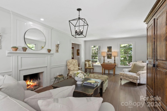 living room featuring ornamental molding, dark wood-type flooring, a brick fireplace, and a chandelier