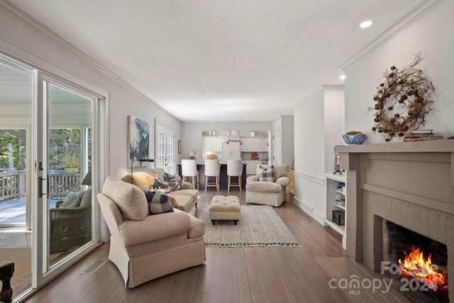 living room featuring wood-type flooring, ornamental molding, and a brick fireplace