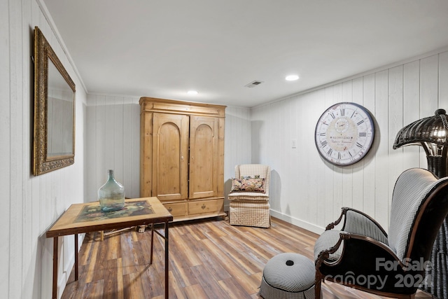 sitting room with light wood-type flooring, wood walls, and ornamental molding