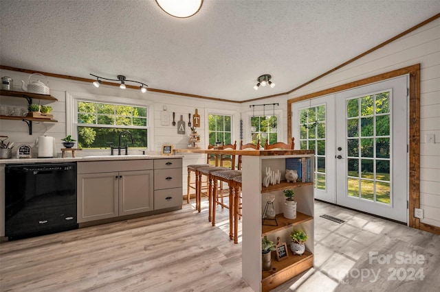 kitchen with black dishwasher, light hardwood / wood-style flooring, sink, lofted ceiling, and wooden walls