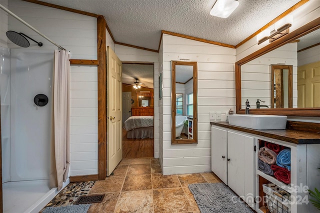 bathroom with a shower with shower curtain, wooden walls, vaulted ceiling, vanity, and a textured ceiling