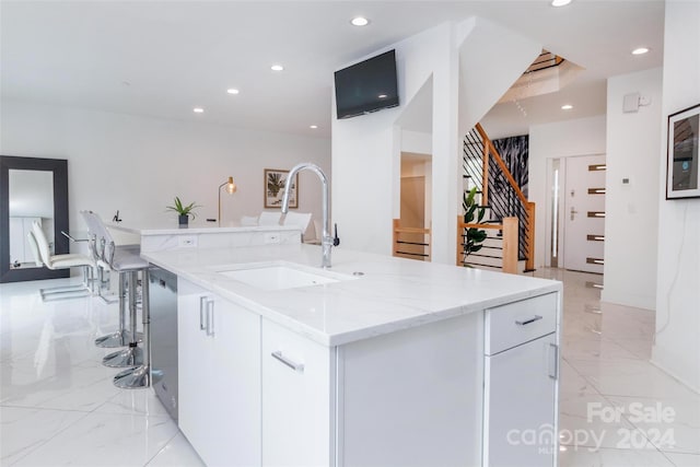 kitchen featuring light stone countertops, white cabinets, a kitchen island with sink, and sink