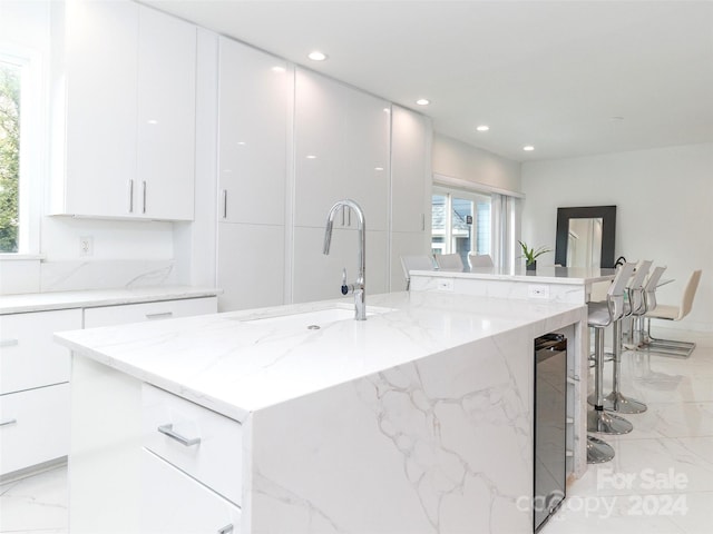 kitchen featuring light stone countertops, sink, an island with sink, and white cabinets