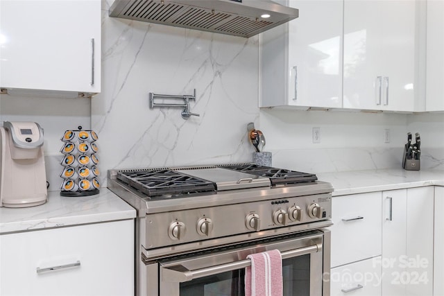 kitchen with light stone counters, tasteful backsplash, wall chimney exhaust hood, white cabinetry, and stainless steel range