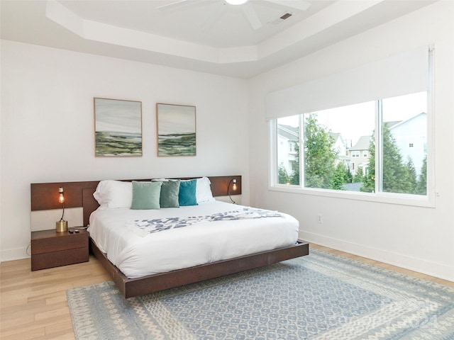 bedroom with ceiling fan, a tray ceiling, and light hardwood / wood-style floors