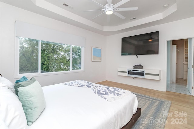 bedroom with light hardwood / wood-style floors, ceiling fan, and a tray ceiling