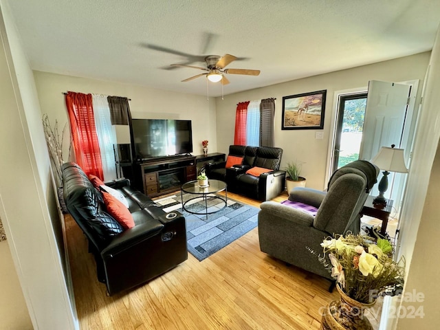 living room with light wood-type flooring, ceiling fan, and a textured ceiling