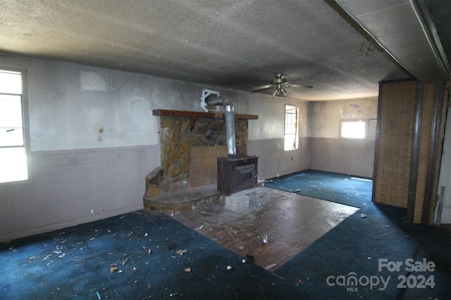 interior space with a textured ceiling, plenty of natural light, ceiling fan, and a wood stove