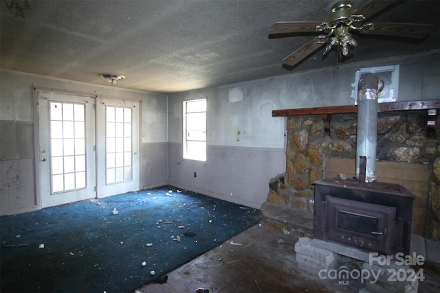 unfurnished living room with ceiling fan, a wood stove, and a textured ceiling