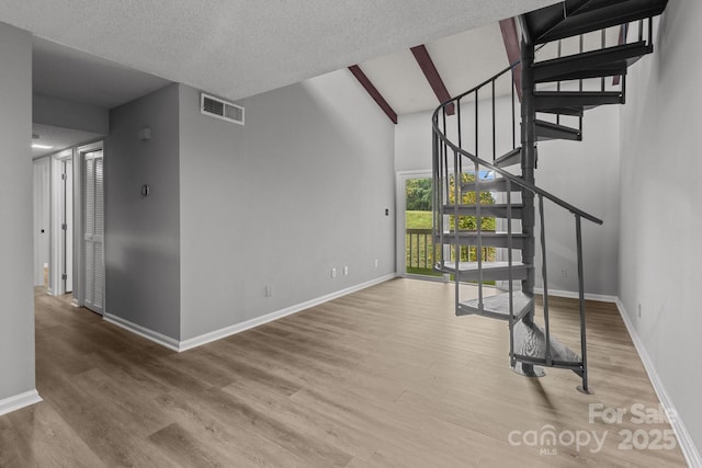 unfurnished living room with hardwood / wood-style flooring, a textured ceiling, and lofted ceiling with beams