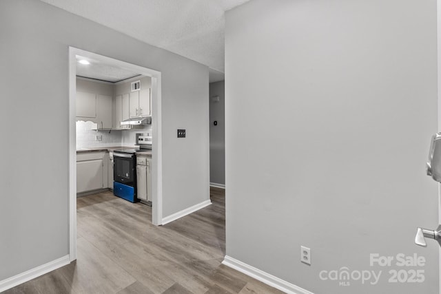 hallway with a textured ceiling and light hardwood / wood-style flooring