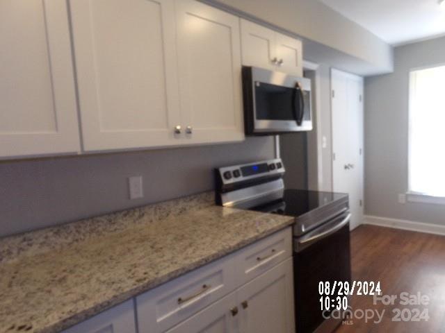 kitchen featuring white cabinets, dark hardwood / wood-style floors, light stone countertops, and stainless steel appliances