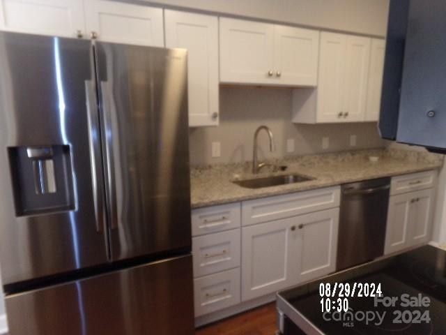 kitchen with white cabinets, stainless steel appliances, light stone counters, and sink