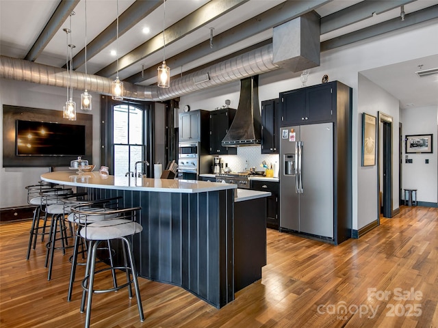 kitchen with light countertops, appliances with stainless steel finishes, light wood-type flooring, premium range hood, and a kitchen breakfast bar