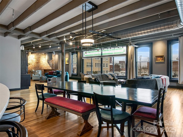 dining space featuring rail lighting, wood finished floors, and beamed ceiling