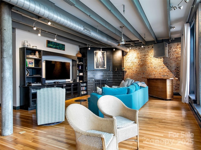 living room featuring rail lighting, a fireplace, brick wall, and wood finished floors