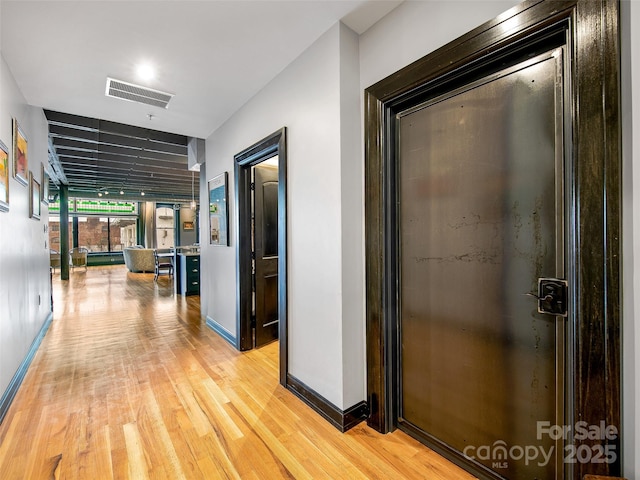 corridor featuring light wood finished floors, baseboards, and visible vents