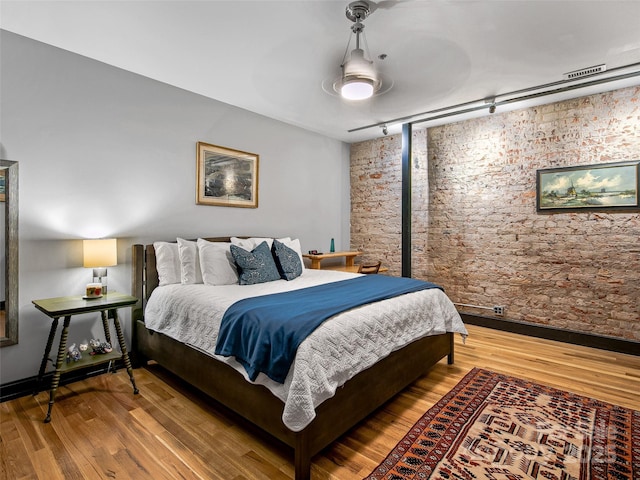 bedroom with rail lighting, brick wall, and wood finished floors