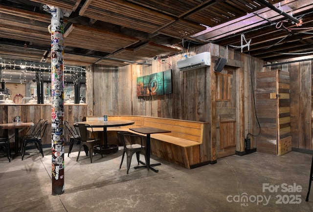 unfinished basement featuring wooden walls, indoor wet bar, and an AC wall unit