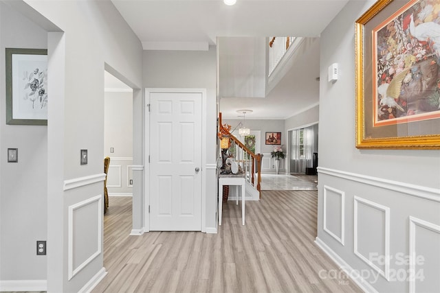 corridor with a wainscoted wall, stairs, light wood-type flooring, and a decorative wall