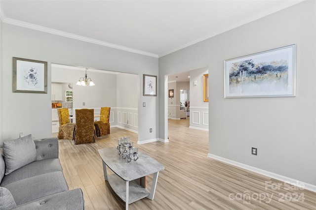 living area with light wood finished floors, a wainscoted wall, ornamental molding, and an inviting chandelier