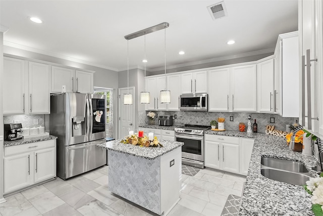 kitchen featuring white cabinets, appliances with stainless steel finishes, light stone countertops, pendant lighting, and a kitchen island