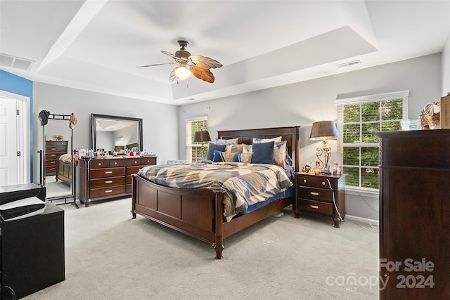 bedroom with ceiling fan, light carpet, and a tray ceiling