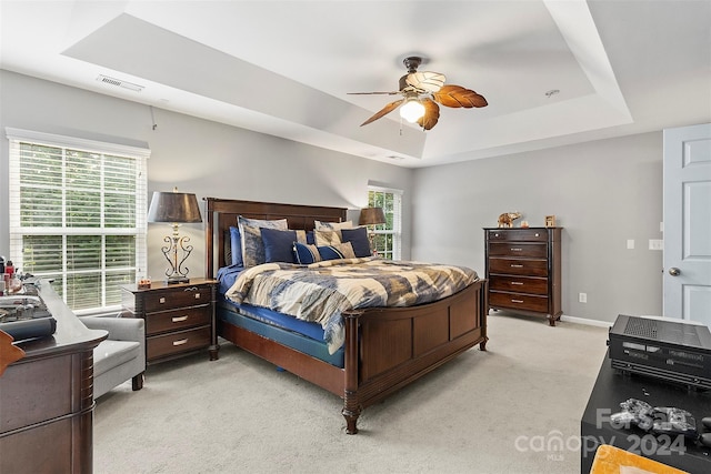 bedroom with light colored carpet, a raised ceiling, and ceiling fan