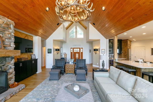 living room with wooden ceiling, light hardwood / wood-style flooring, a stone fireplace, high vaulted ceiling, and a chandelier