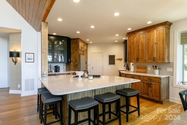 kitchen with a kitchen bar, stainless steel appliances, light wood-type flooring, and a kitchen island with sink