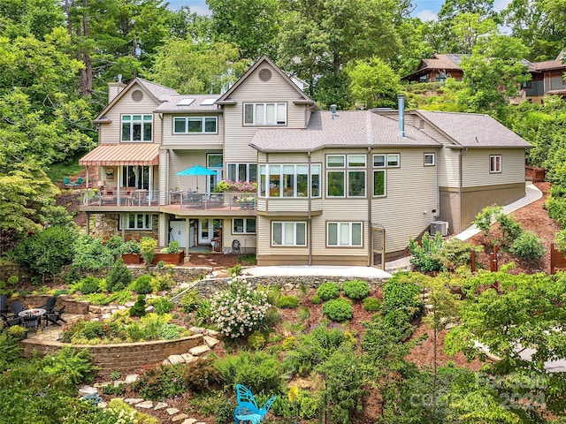 back of house with a shingled roof, an outdoor fire pit, a chimney, stone siding, and a patio