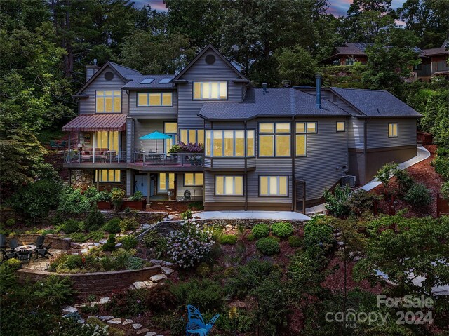 back house at dusk featuring a patio, a balcony, and central air condition unit