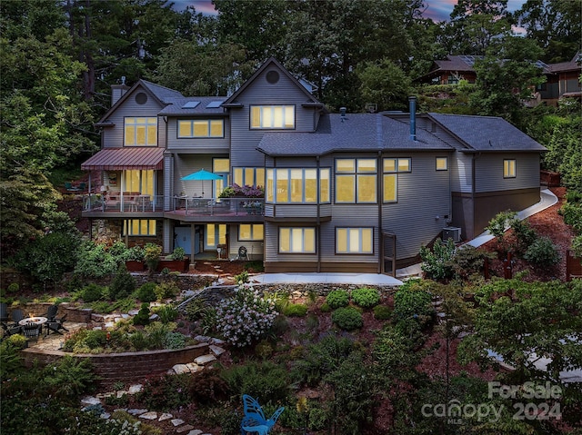 back of house at dusk featuring a patio area, a chimney, and a fire pit