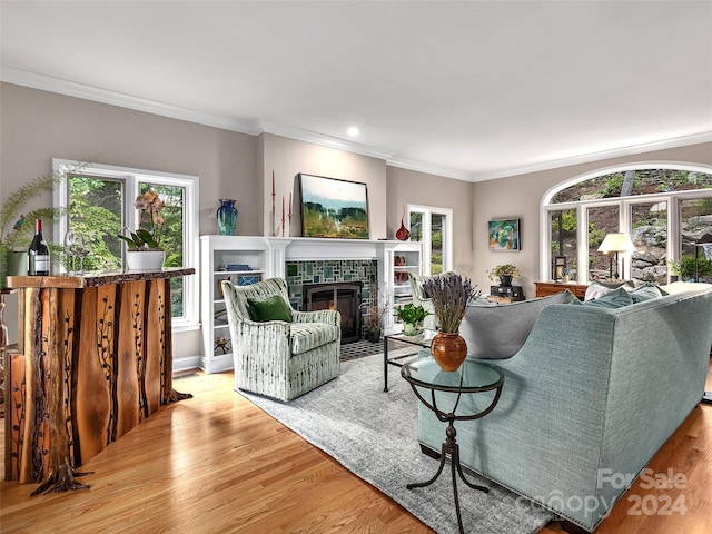 living room featuring a tiled fireplace, ornamental molding, plenty of natural light, and light hardwood / wood-style flooring