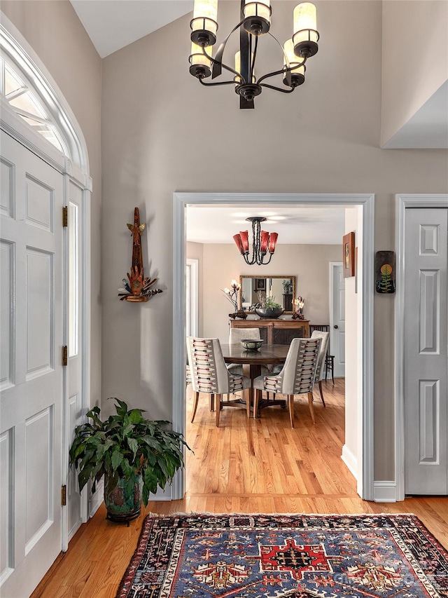 entrance foyer featuring light wood-type flooring, a notable chandelier, and vaulted ceiling