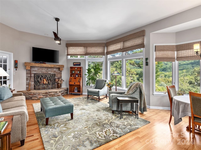 living area featuring a stone fireplace, baseboards, and wood finished floors