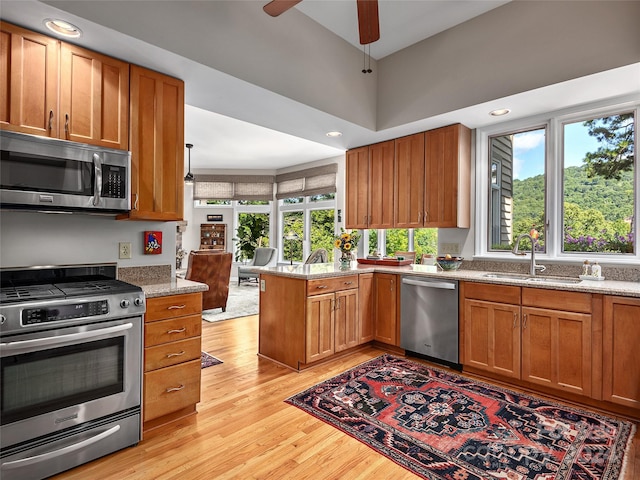 kitchen with light hardwood / wood-style flooring, stainless steel appliances, sink, kitchen peninsula, and ceiling fan