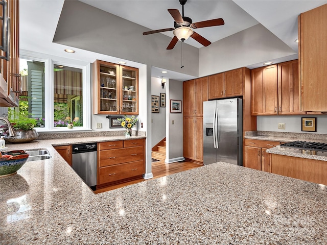 kitchen with light stone counters, stainless steel appliances, light hardwood / wood-style floors, sink, and ceiling fan