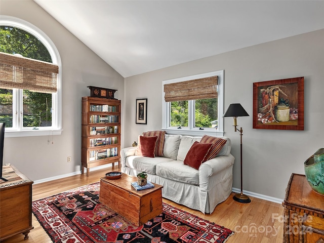 living area featuring baseboards, light wood-style floors, and lofted ceiling