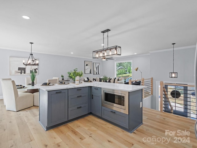 kitchen with pendant lighting, a kitchen island, stainless steel microwave, gray cabinetry, and light hardwood / wood-style floors