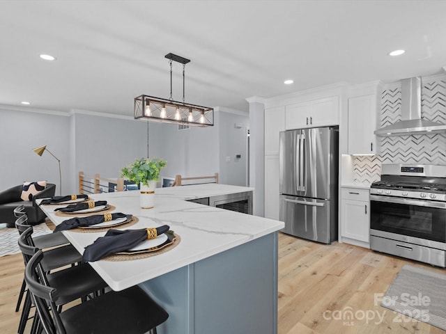 kitchen featuring white cabinets, appliances with stainless steel finishes, wall chimney range hood, decorative backsplash, and hanging light fixtures