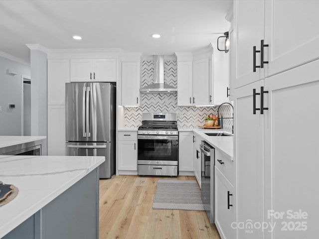 kitchen with white cabinetry, appliances with stainless steel finishes, ornamental molding, wall chimney exhaust hood, and sink