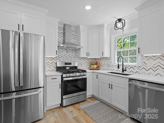 kitchen with stainless steel appliances, sink, white cabinetry, and wall chimney range hood