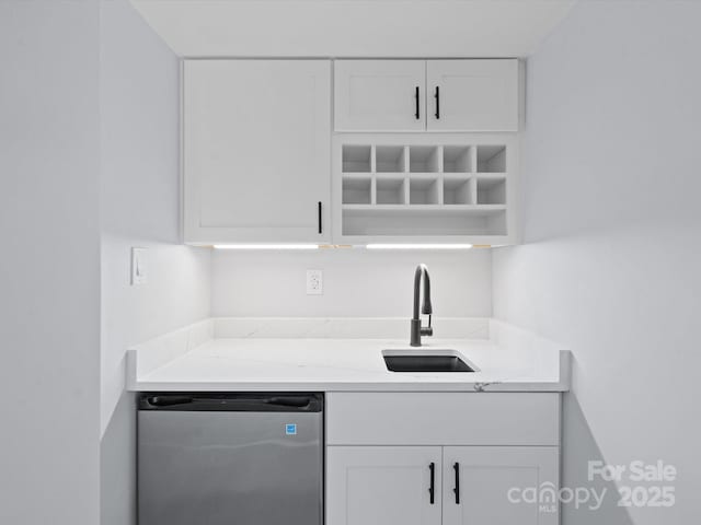 kitchen with light stone countertops, white cabinetry, dishwasher, and sink