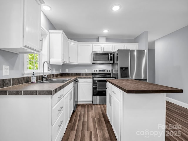 kitchen featuring a center island, appliances with stainless steel finishes, white cabinetry, a sink, and wood counters