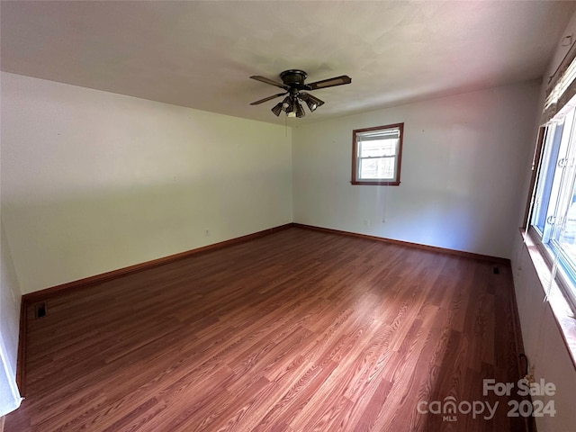 unfurnished room featuring dark wood finished floors, a ceiling fan, and baseboards