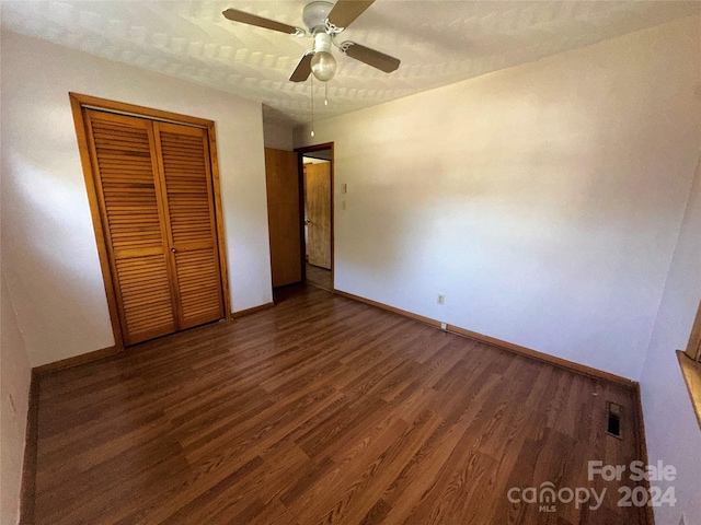 unfurnished bedroom featuring wood finished floors, visible vents, baseboards, ceiling fan, and a closet