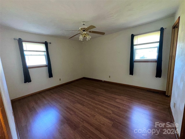 unfurnished room with a wealth of natural light, dark wood-type flooring, and baseboards