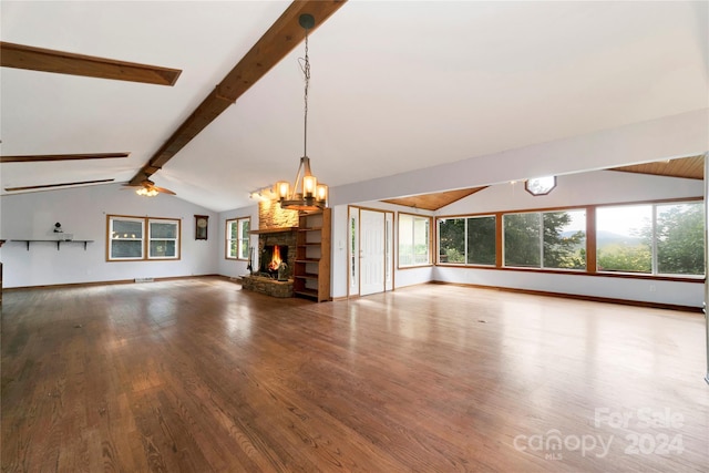 unfurnished living room featuring ceiling fan with notable chandelier, wood-type flooring, lofted ceiling with beams, and a stone fireplace